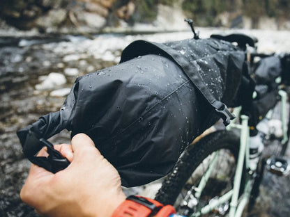 Person adjusting a black topeak bikepacking bag on a bicycle by a river